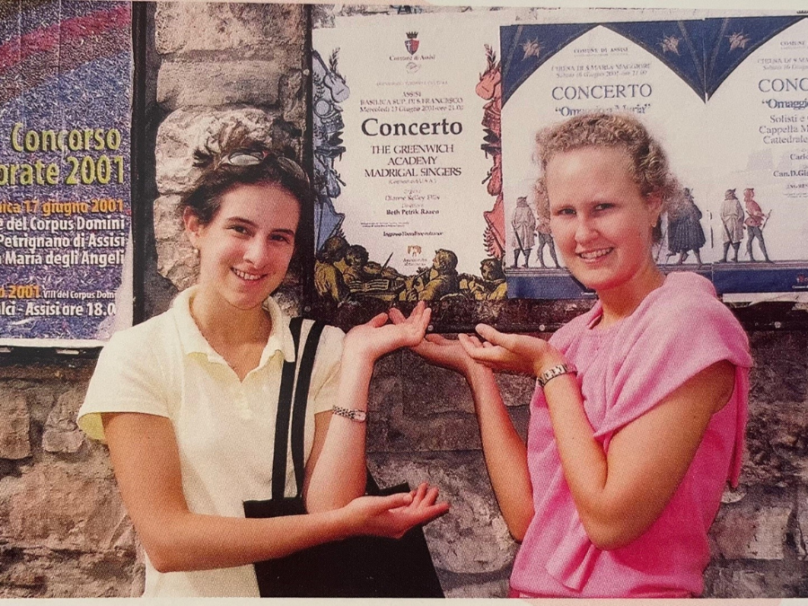 Two girls standing in front a concert poster and proudly pointing to it