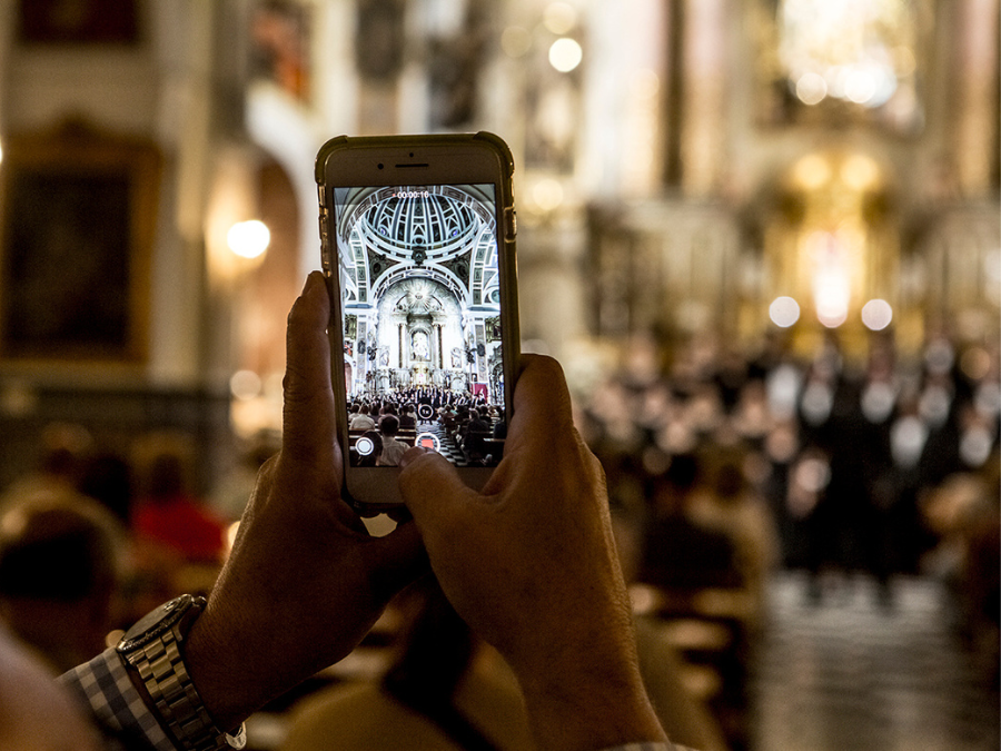 Hands holding a smartphone as it records a video of a choir singing in a church