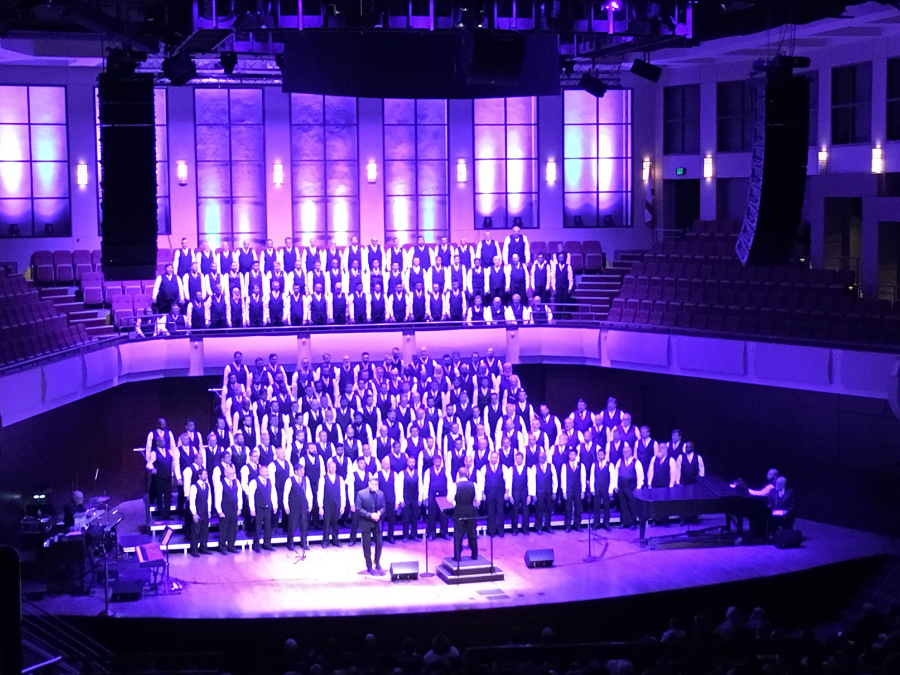 Men's choir performing on stage while bathed in purple lights