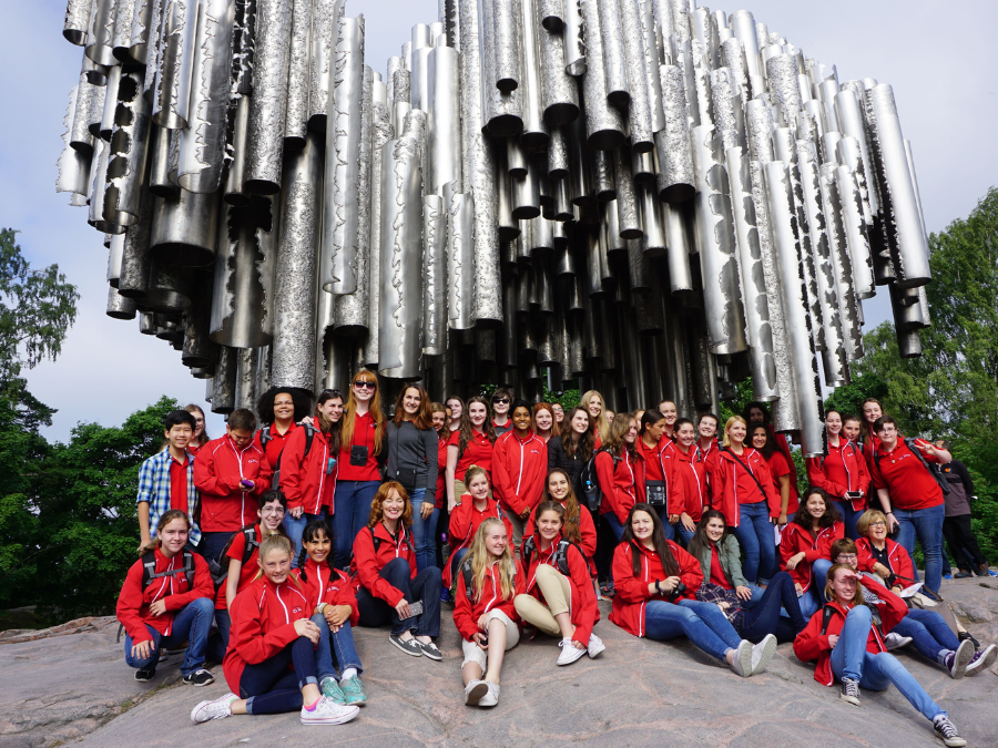 A group of students in red jackets sitting on a rock and gathered in front of the Sibelius Statue in Helsinki, Finland