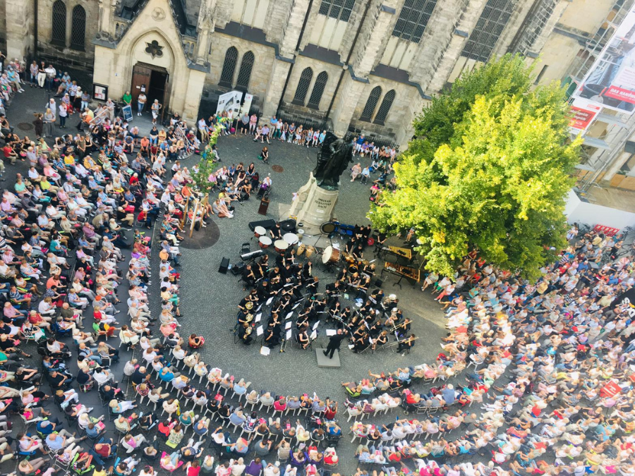 An orchestra playing in front of a statue of Bach surrounded by an audience in Leipzig, Germany